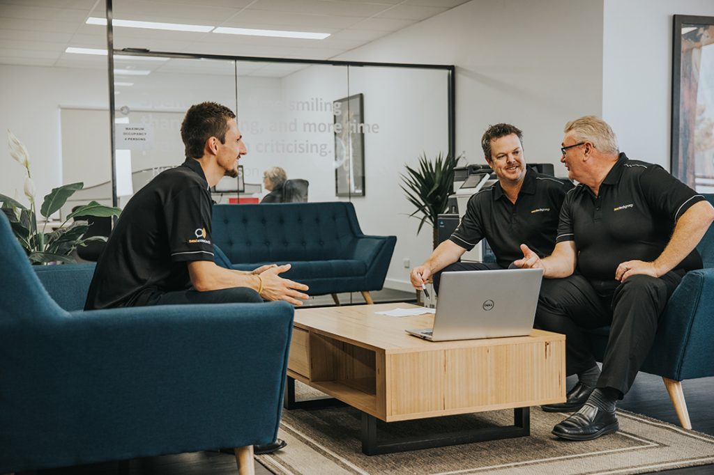 Three men having a meeting in an office lounge area with a laptop