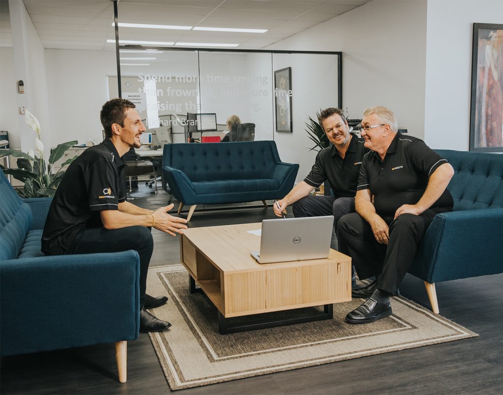Three men in black polo shirts having a meeting in an office lounge area