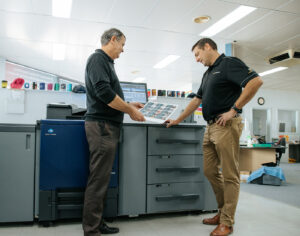 2 men looking down at a printed sheet of paper in front of a production printer