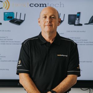 man in next tech group uniform in front of interactive screen looking at camera